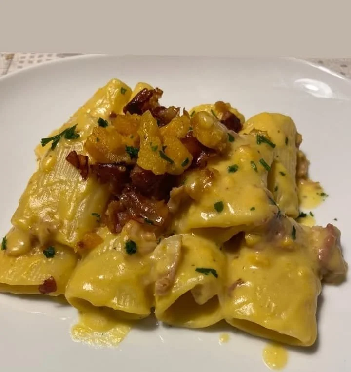 Paccheri con crema di zucca e speck serviti in un piatto bianco