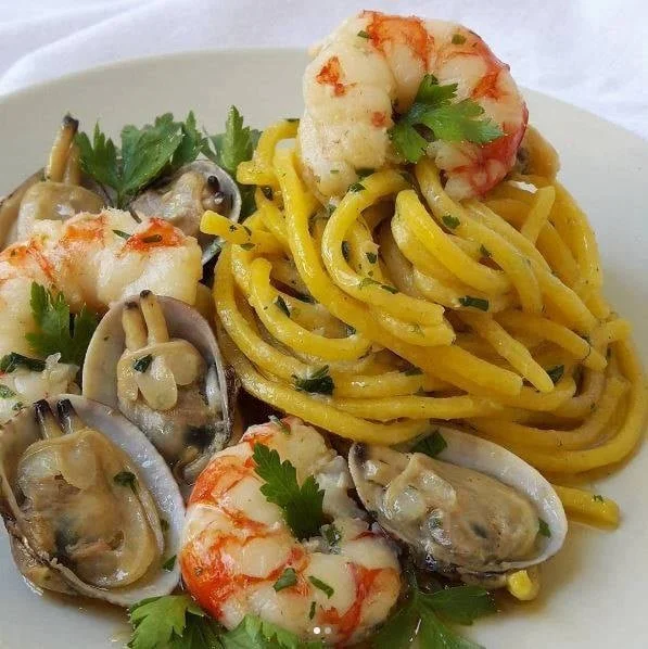 Spaghetti alla Chitarra con Vongole Veraci e Gamberi serviti in un piatto gourmet.